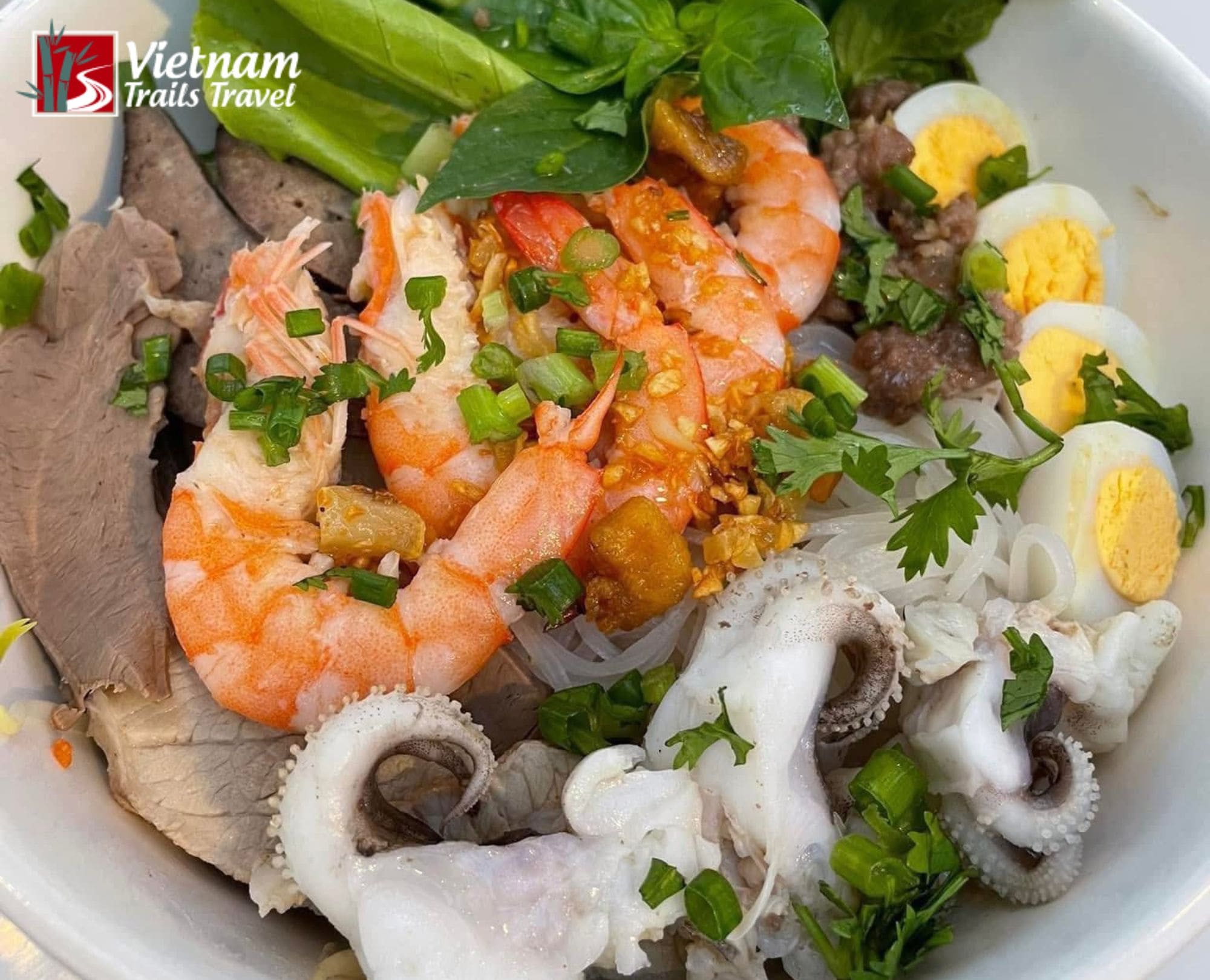 A colorful bowl of authentic Hu Tieu Nam Vang with seafood and pork toppings, served with fresh Vietnamese herbs