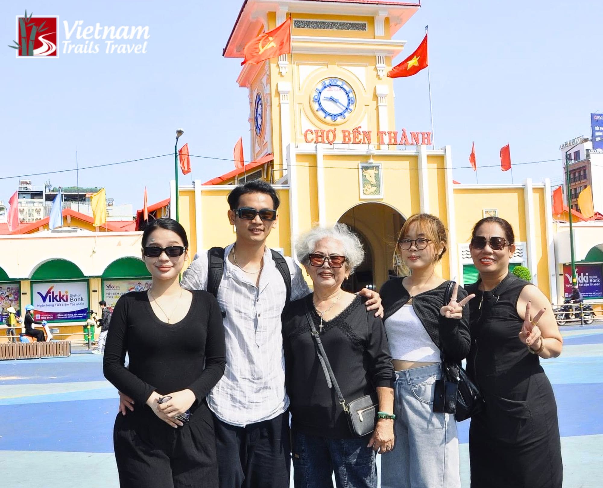 A family group smiling in front of the historic Ben Thanh Market clock tower