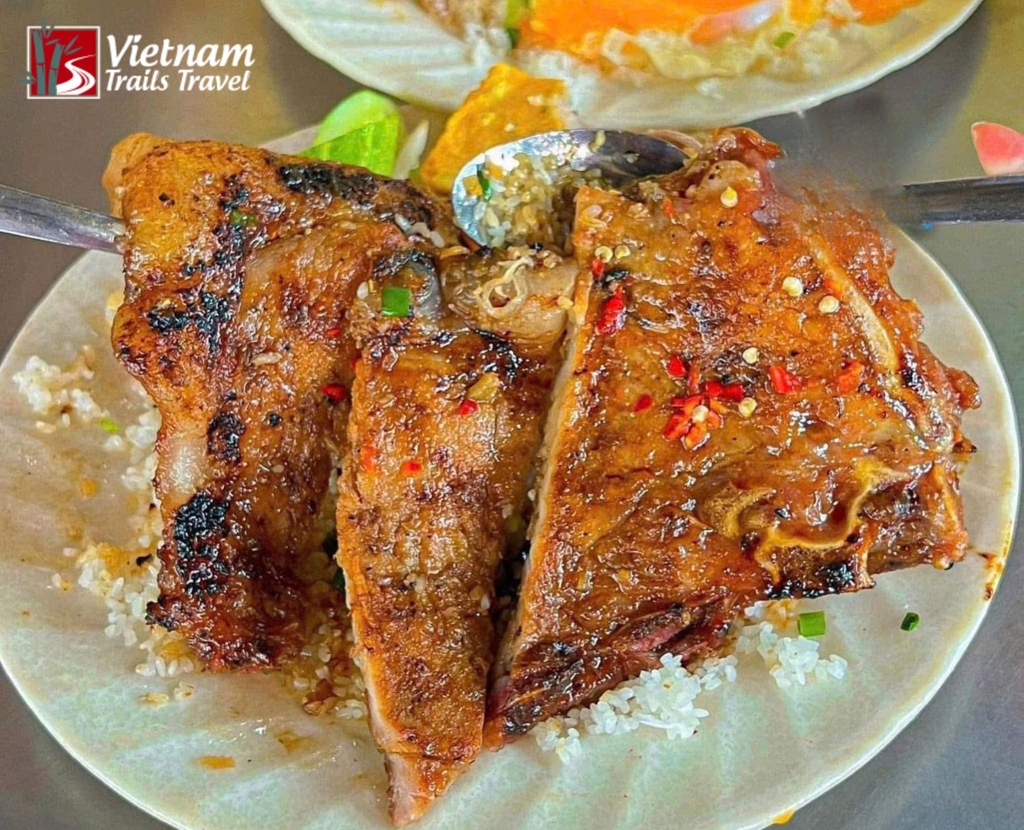 A plate of Vietnamese broken rice (Com Tam) featuring a grilled pork chop, shredded pork skin (bi), a steamed egg meatloaf (cha), and a fried egg