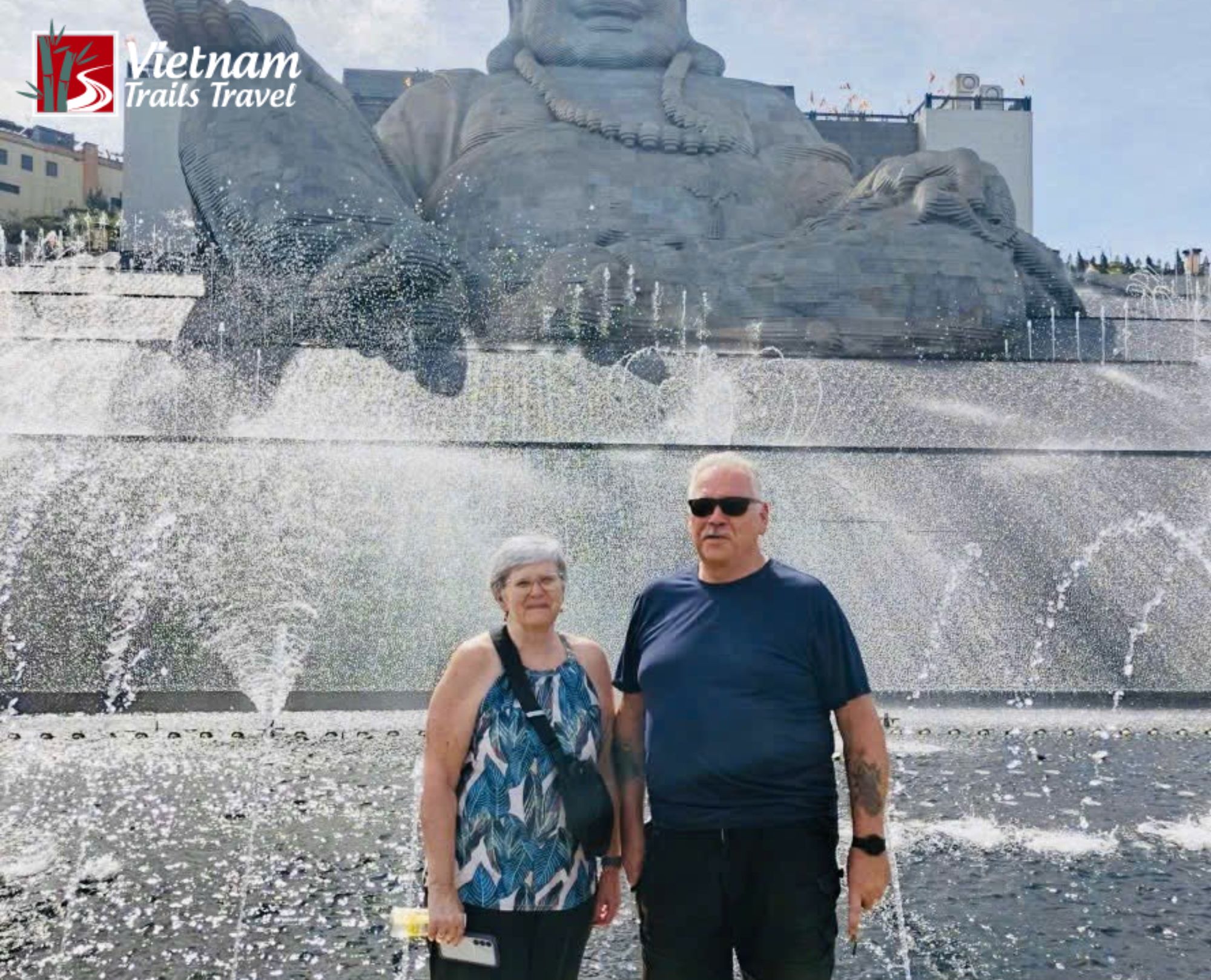 Senior travelers posing in front of the giant Maitreya Buddha statue and waterfall feature during a Ba Den Mountain tour