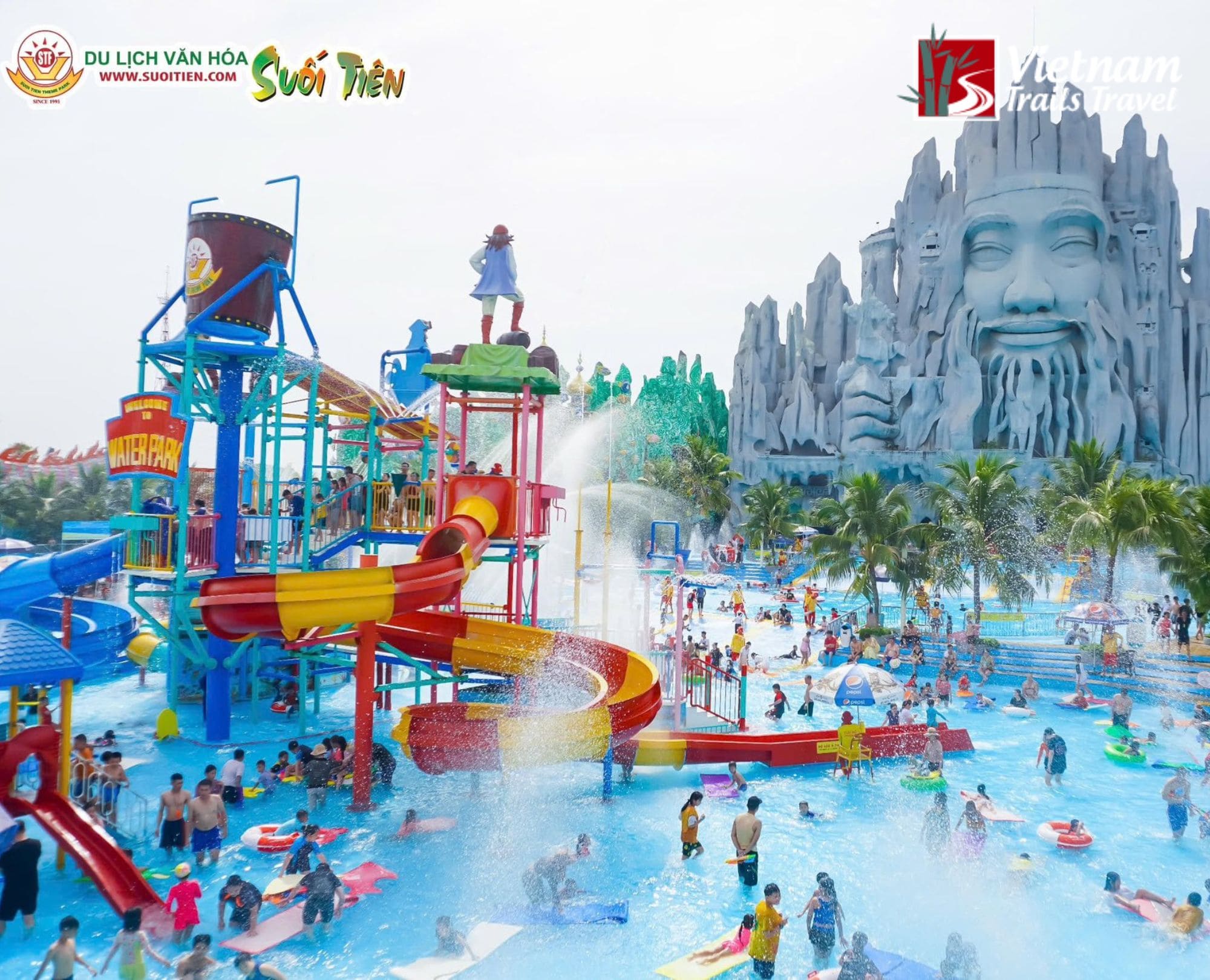 The iconic giant mythical mountain face overlooking a busy water park area with slides and fountains at Suoi Tien