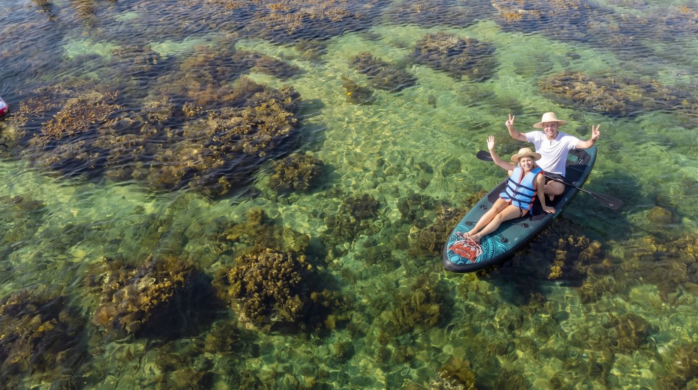 A couple enjoying stand-up paddleboarding (SUP) over a vibrant coral reef in clear blue water at Hon Kho