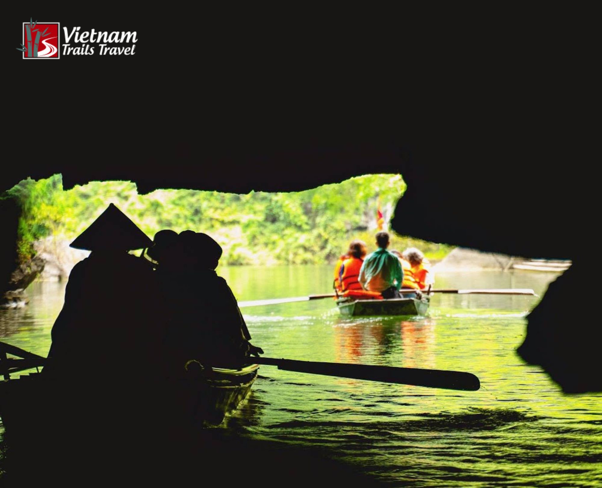 Boat tour emerging from limestone cave onto scenic river surrounded by tropical greenery in Ninh Binh