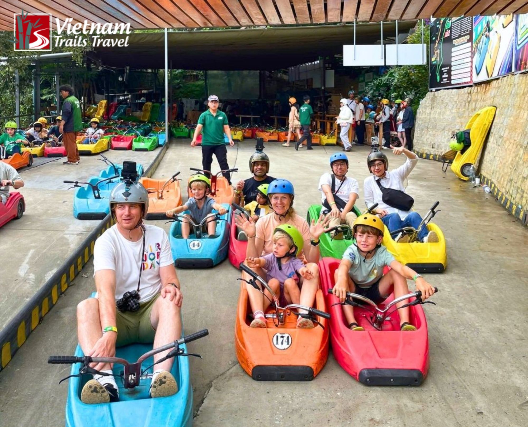 Family and kids riding colorful downhill go-karts at an amusement park in Dalat
