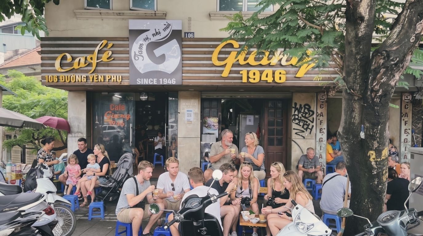 Group of foreign tourists sitting on plastic stools outside the historic Cafe Giang 1946 on Yen Phu Street in Hanoi, enjoying famous Vietnamese egg coffee