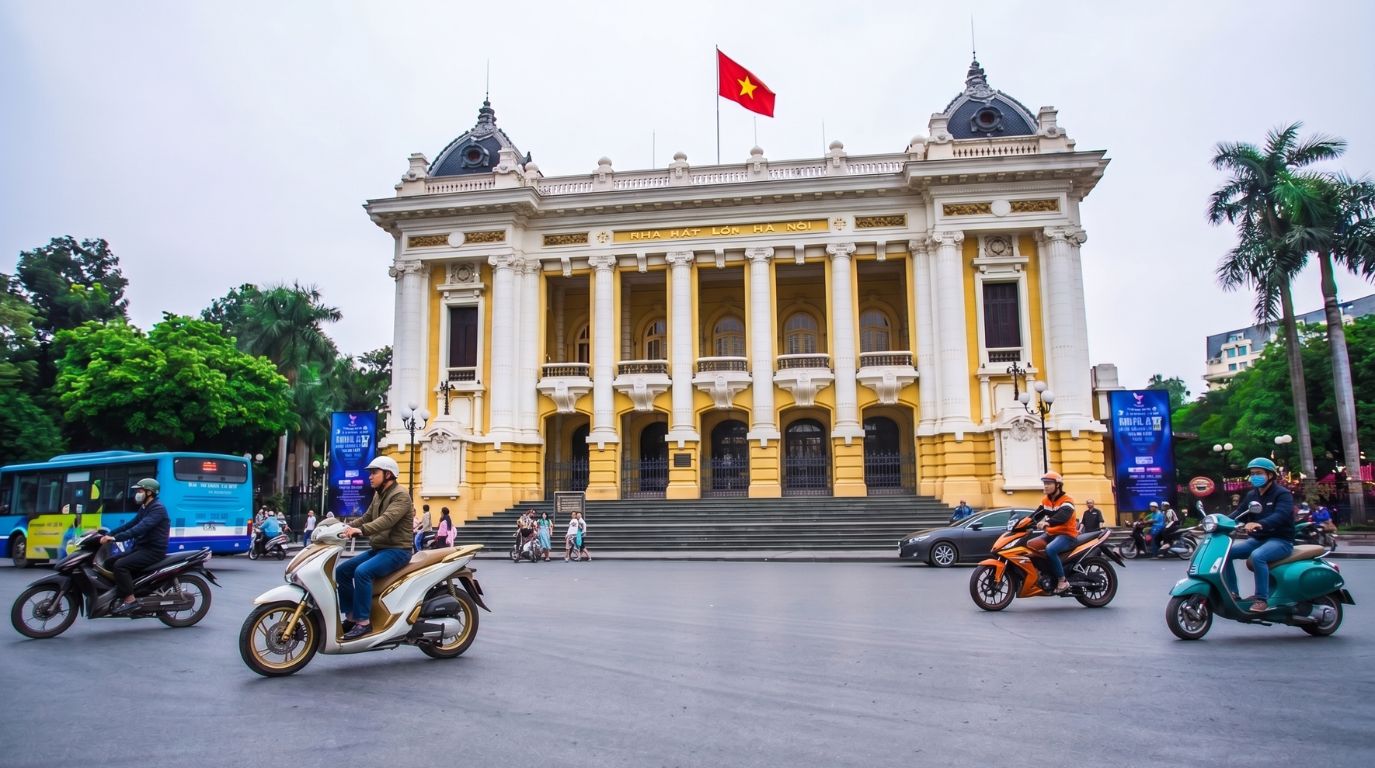 Motorbikes riding past the elegant French colonial architecture of the famous Hanoi Opera House building in the city center