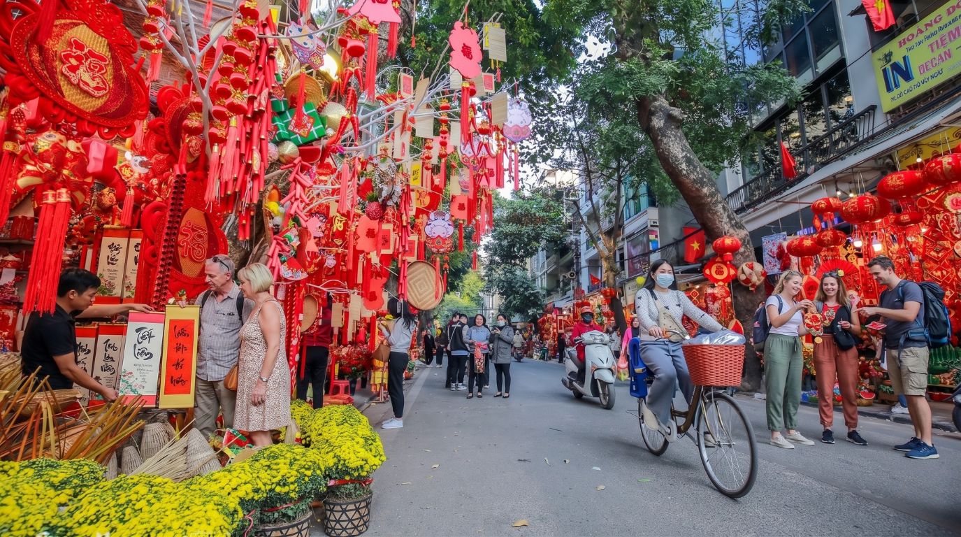 Tourists and locals walking along Hang Ma street in the Hanoi Old Quarter, beautifully decorated with vibrant red lanterns and Tết items