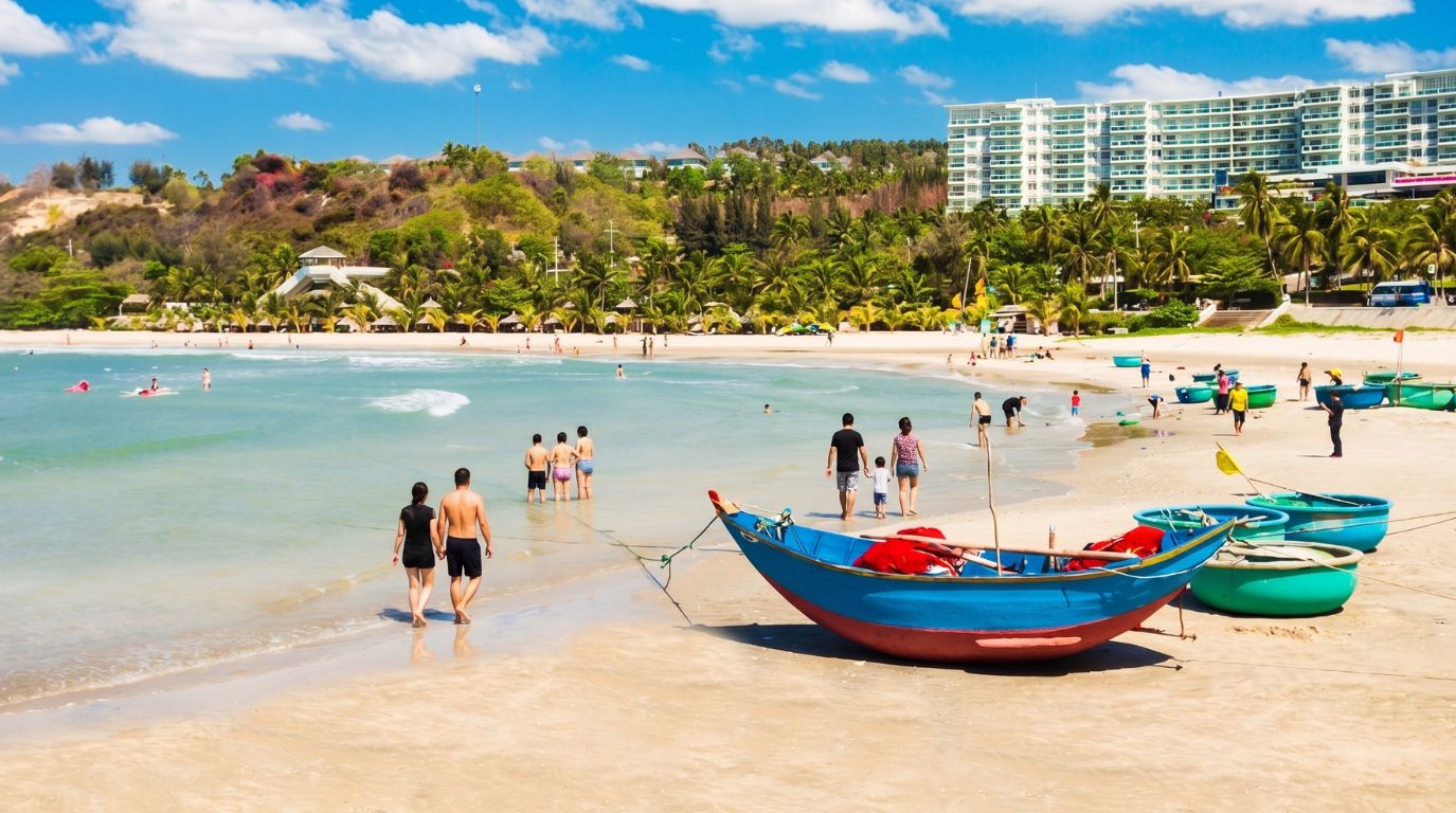 Tourists enjoying a sunny day on a beautiful white sand beach dotted with traditional blue basket boats and luxury coastal resorts