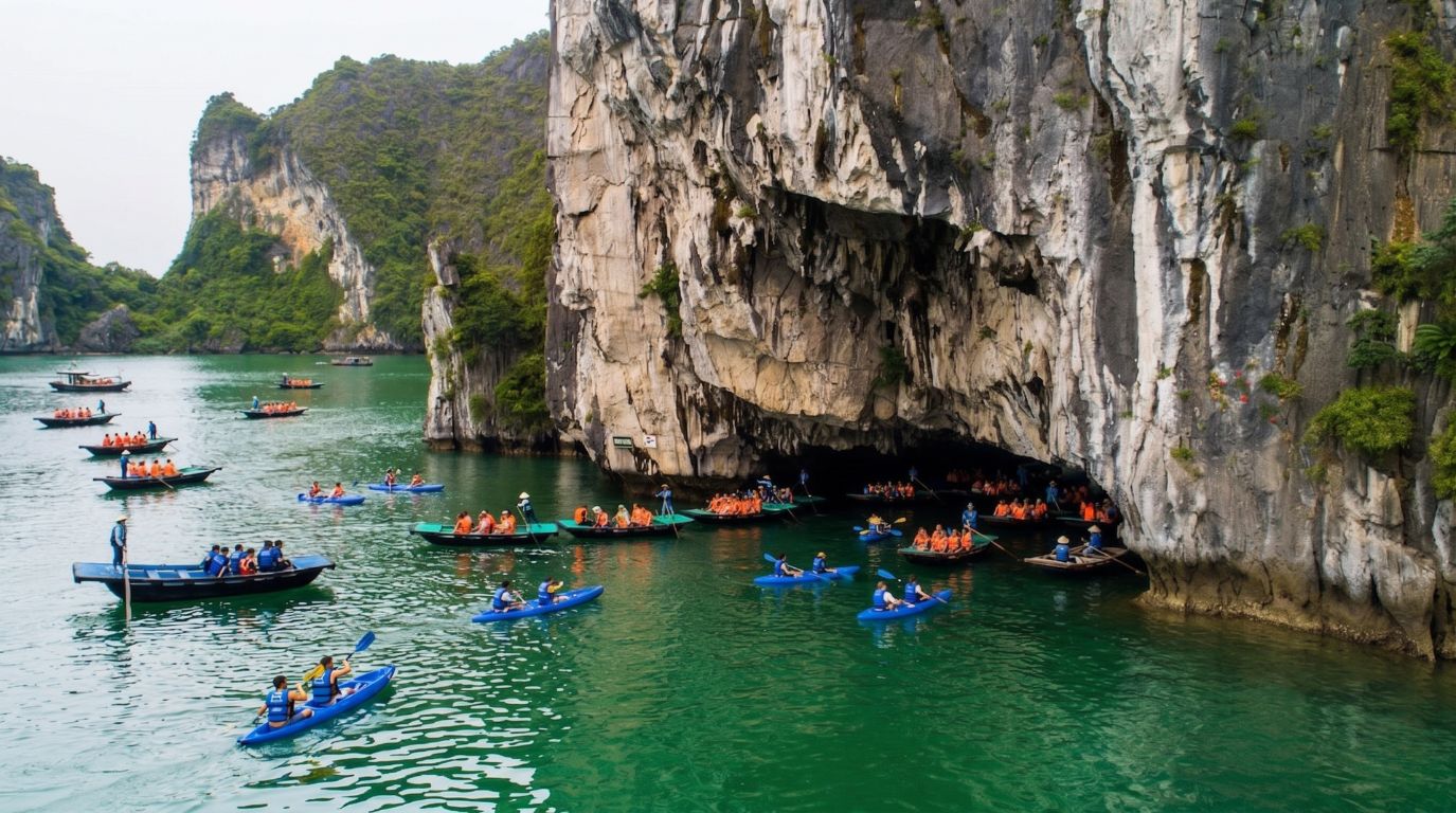 Tourists on traditional bamboo rowboats and kayaks exploring a beautiful water cave beneath a massive limestone karst in Bai Tu Long