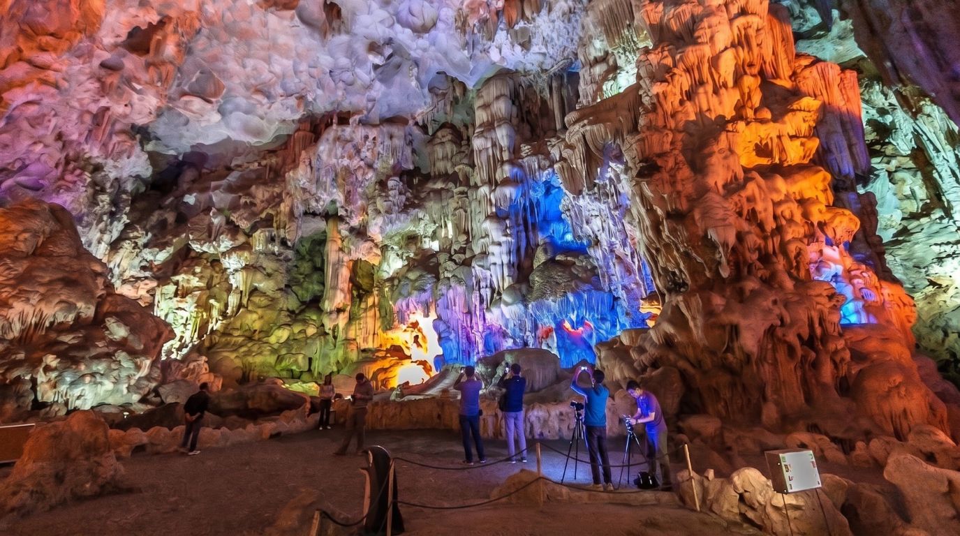 Tourists taking photos of the spectacular stalactites and stalagmites illuminated with colorful lights inside a Halong Bay limestone cave