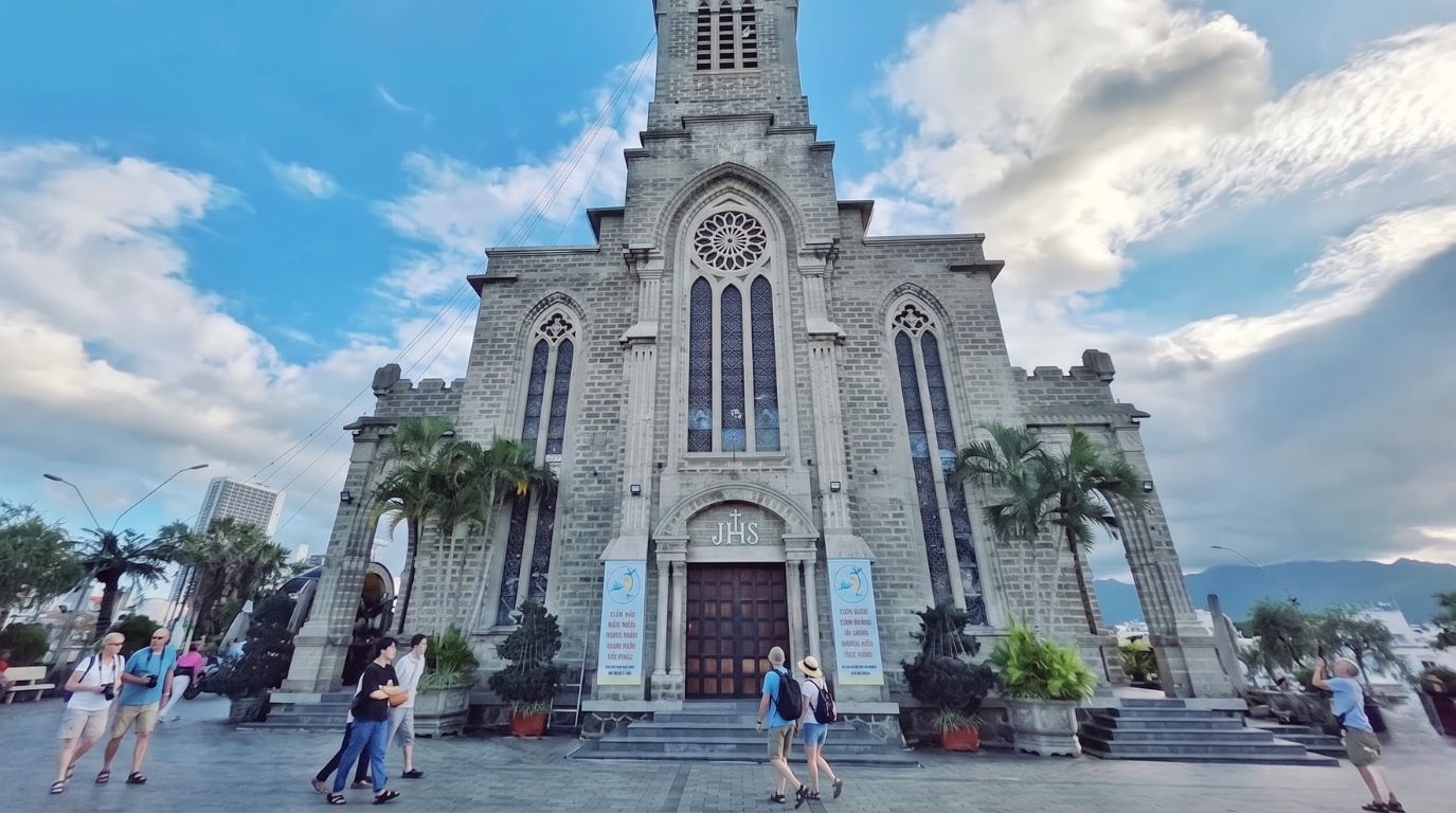 Tourists walking outside the historic Nha Trang Cathedral, also known as the Stone Church, featuring beautiful Gothic architecture.