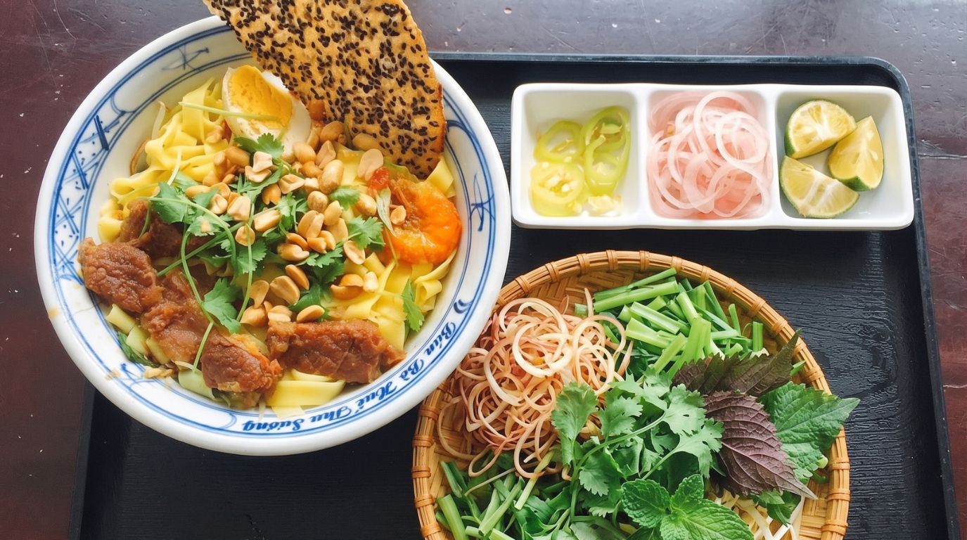 Traditional Mi Quang noodle soup from Central Vietnam accompanied by fresh herbs, lime, and chili
