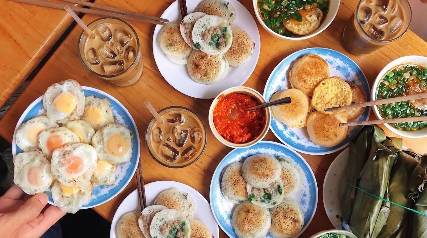 Traditional Nha Trang street food spread featuring crispy Banh Can quail egg pancakes, dipping sauces, and iced coffee