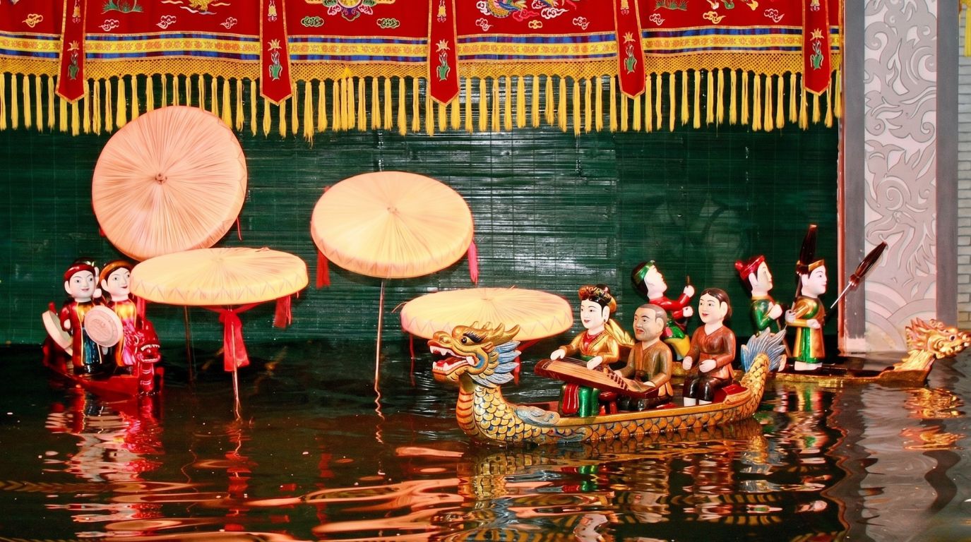 Traditional Vietnamese water puppet show performance featuring colorful wooden figures, boats, and dragons on a water stage in Hanoi