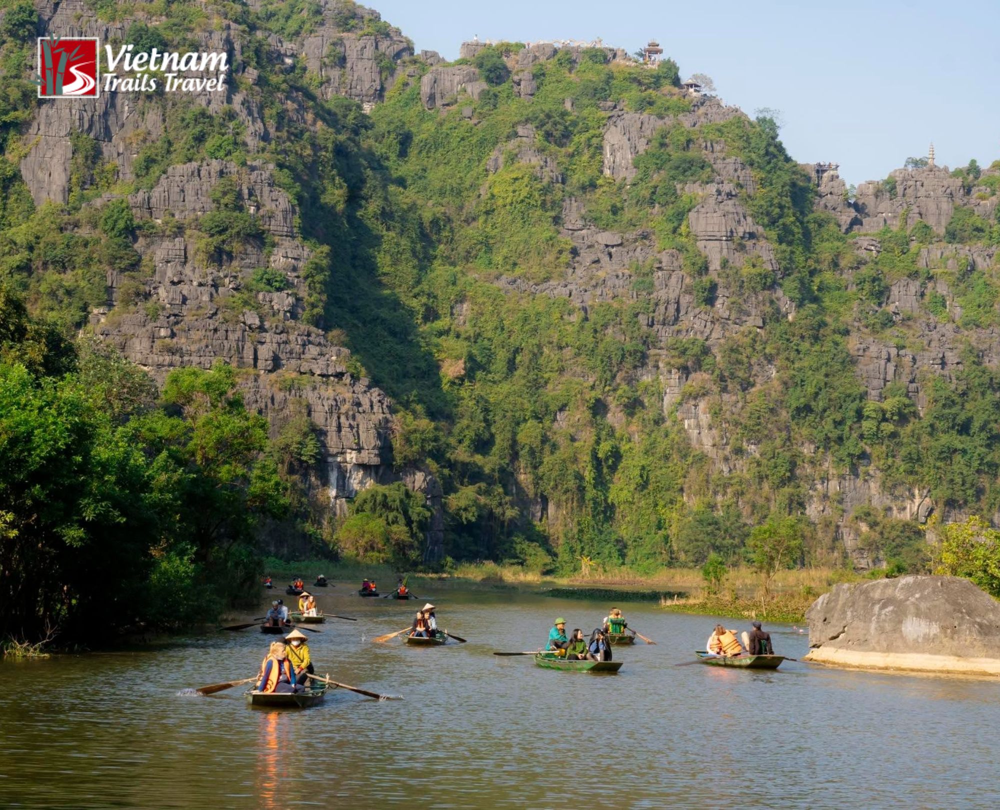 Trang An versus Tam Coc sightseeing boats on calm river surrounded by lush green mountains