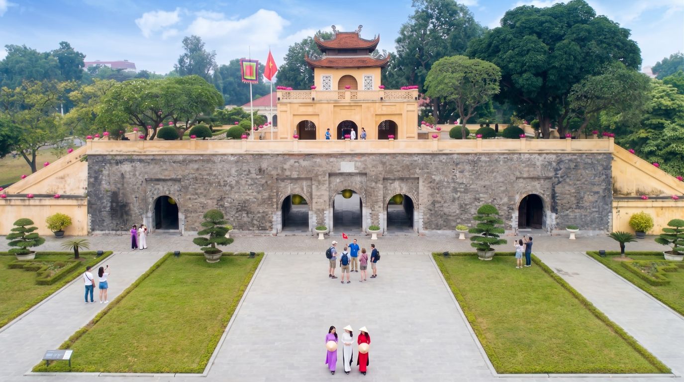 Visitors and women wearing traditional Ao Dai exploring the massive stone gates of the ancient Imperial Citadel of Thang Long in Hanoi