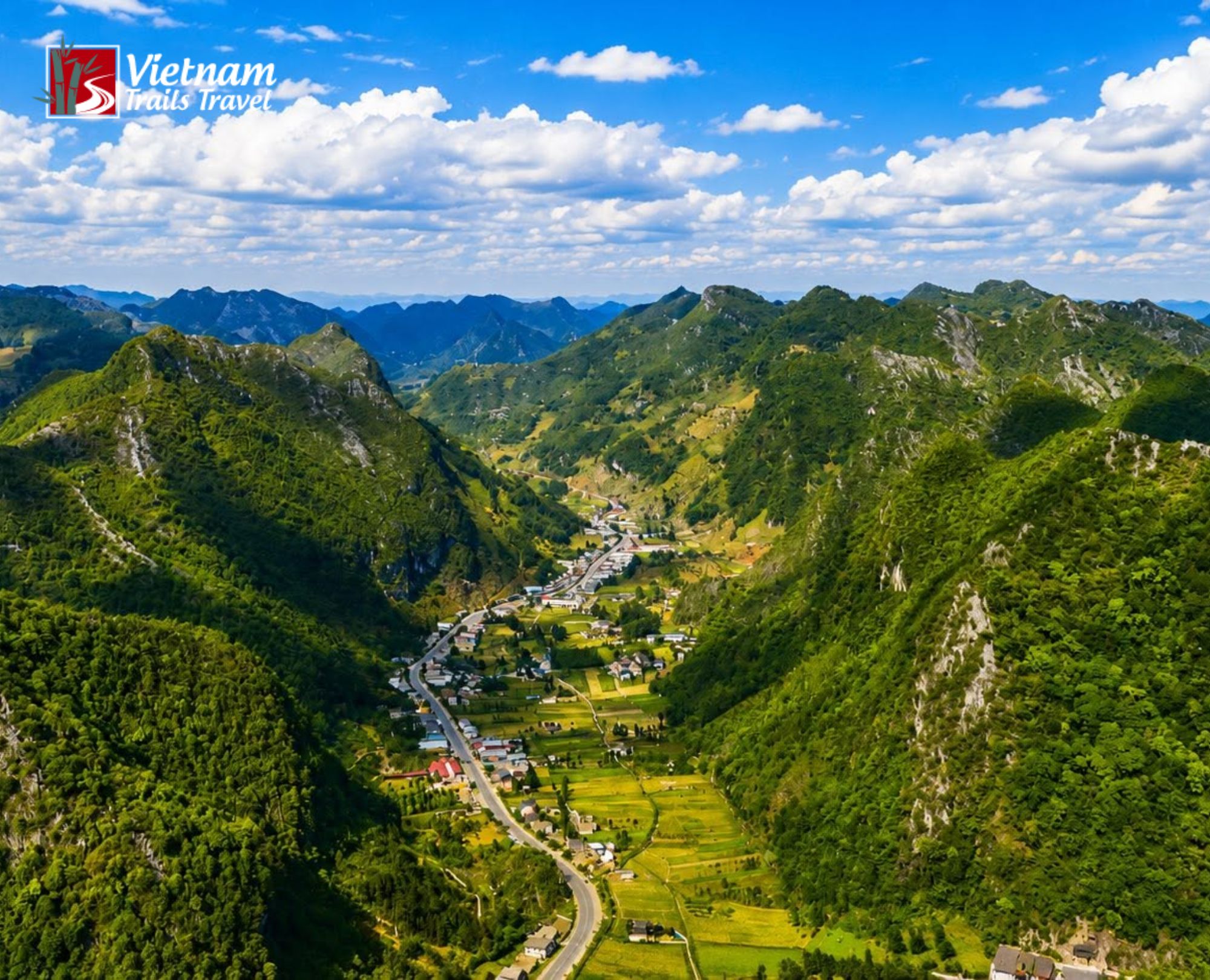 Golden and green cultivated fields stretch across the valley floor, connected by a winding road, with a traditional village nestled between towering mountains