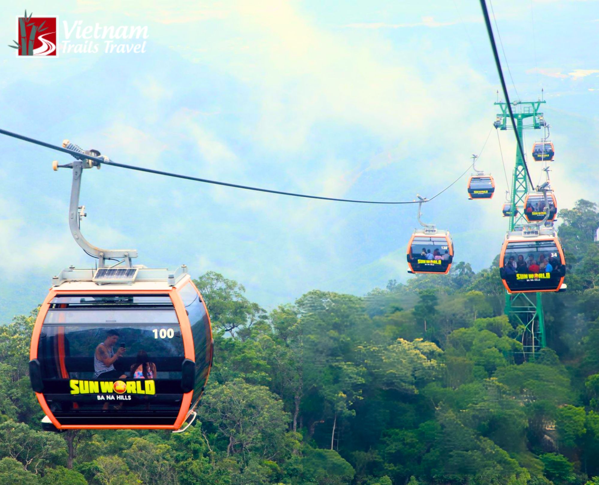 Ba Na Hills cable car system carrying orange and black gondolas through lush green forest and misty sky