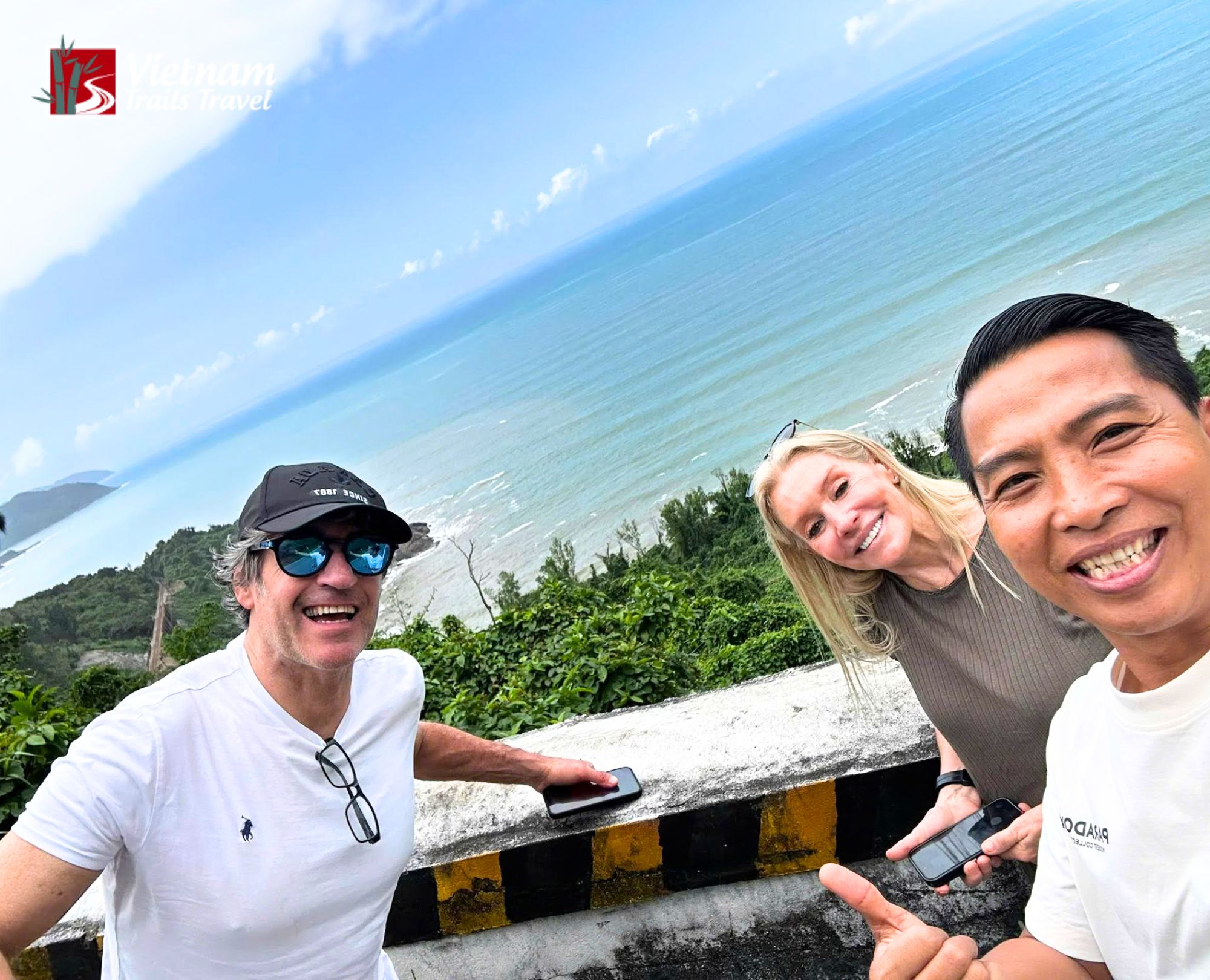 A tour guide taking a joyful selfie with two cruise guests at Lang Co beach during a stop on the way to Da Nang with the stunning blue ocean and green mountains behind them