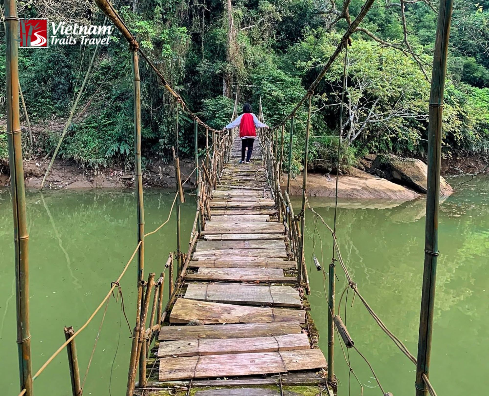 A tourist experiencing the iconic rattan and wood suspension bridge with traditional durable design on the scenic trekking trail leading into Giang Ta Chai village
