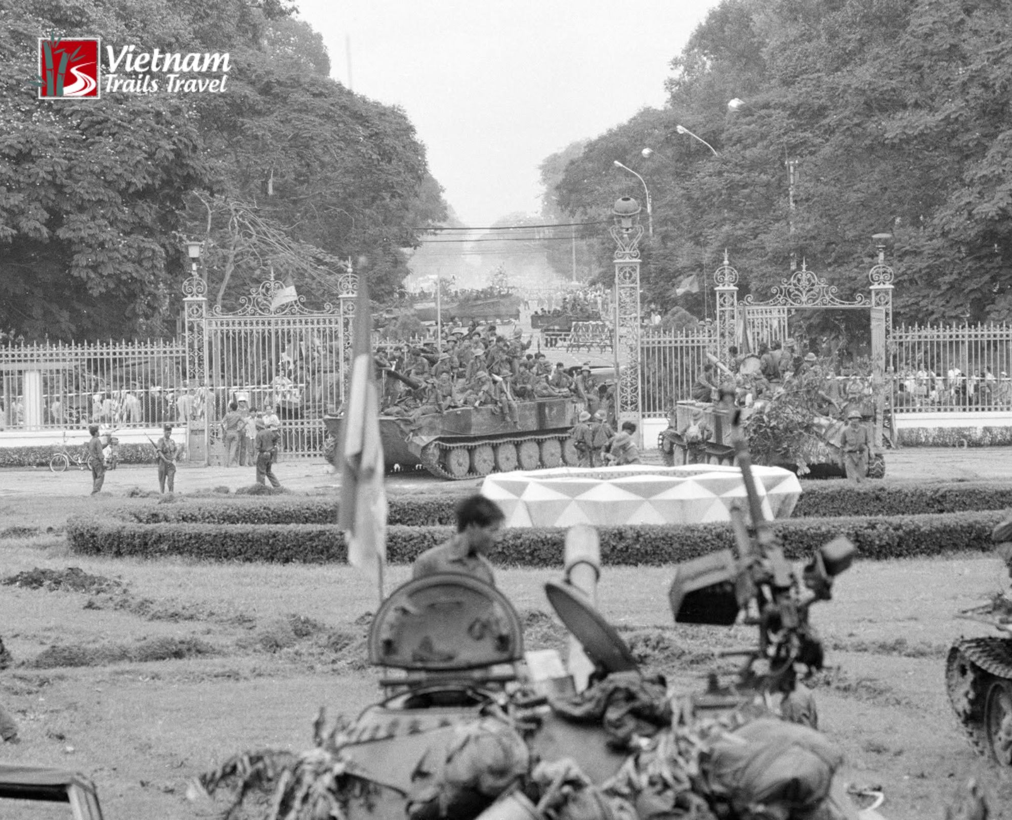 Tank breaking past the palace gate with uniformed soldiers nearby during the pivotal surrender of Saigon in 1975