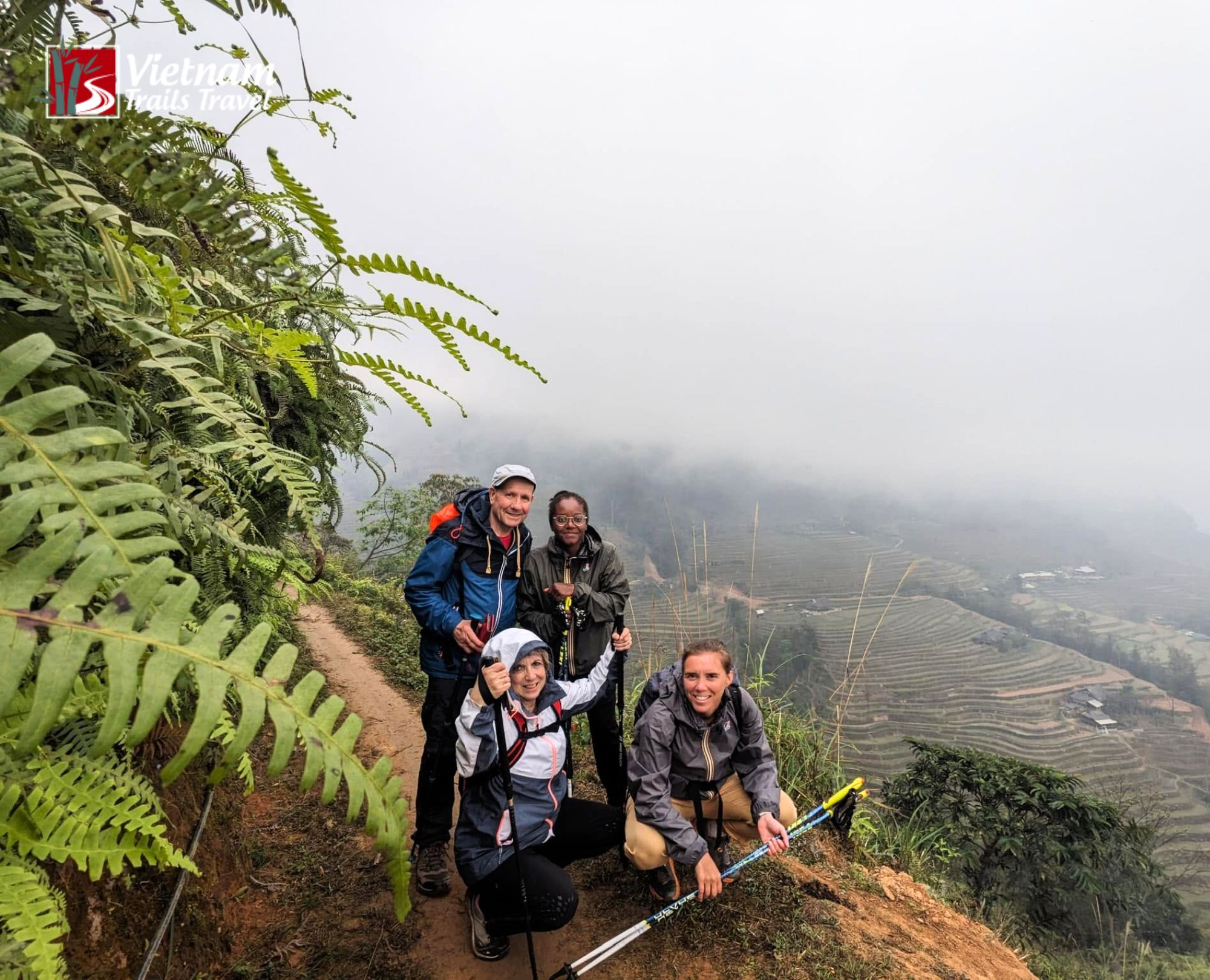 Four travelers on a northern Vietnam itinerary from Hanoi, resting on a fern lined path in the fog