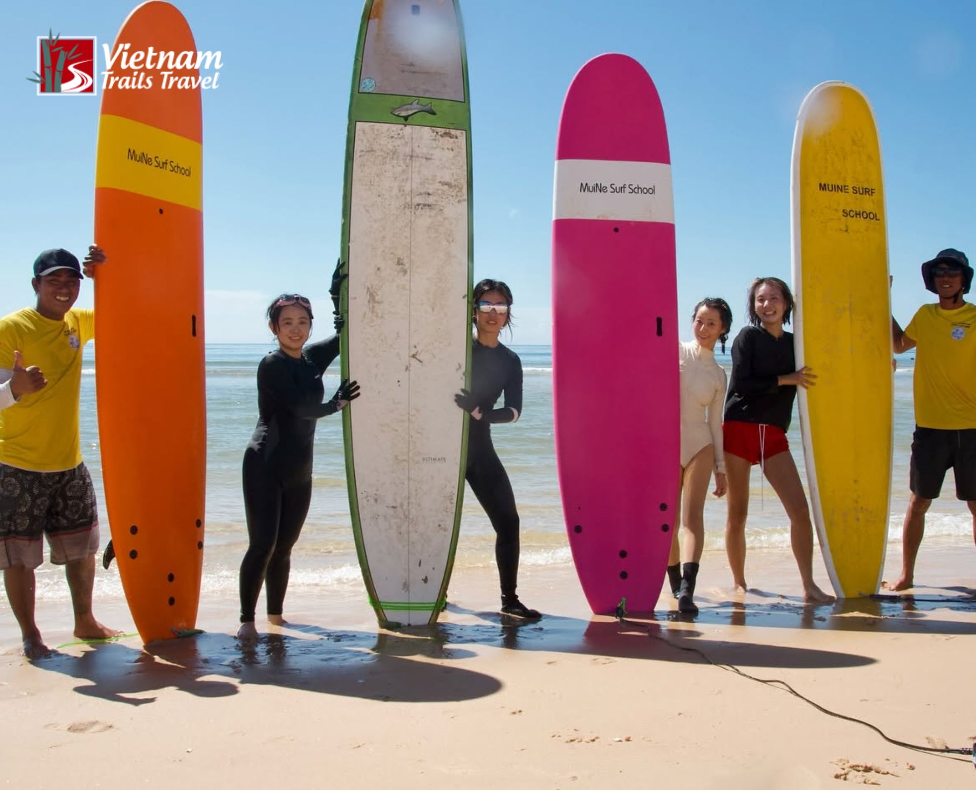 Happy visitors posing with surfboards during beach vacation at Mui Ne Beach