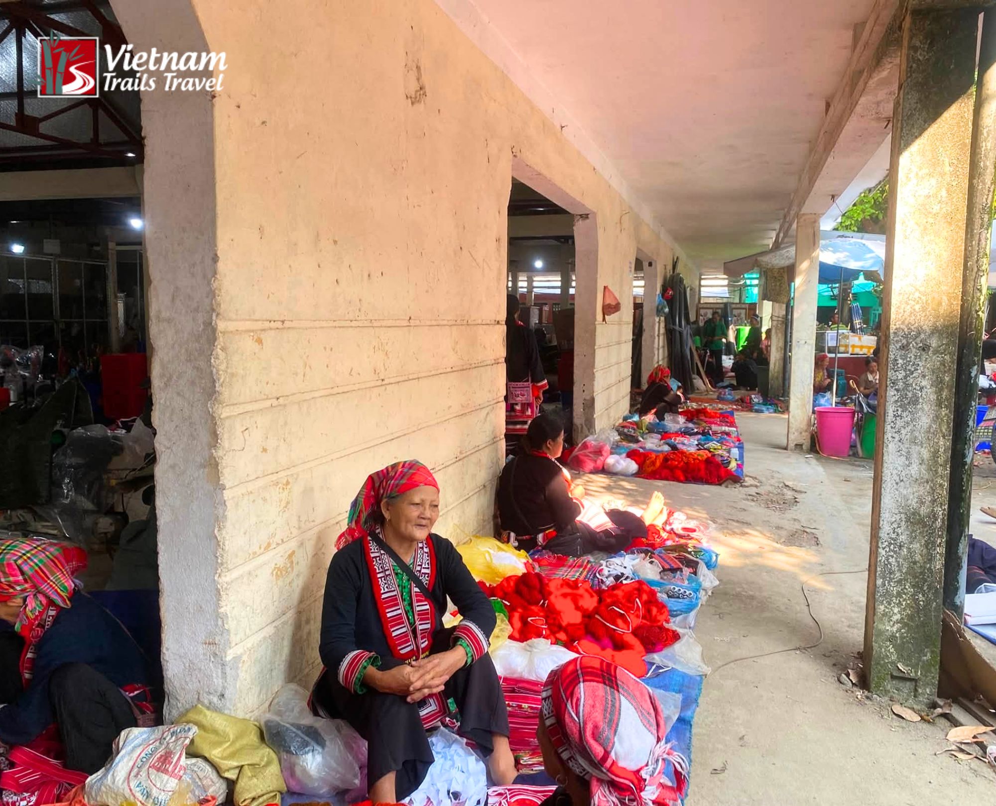 The women in traditional embroidered clothing selling textiles under a covered walkway at Hoang Su Phi market on Sunday morning