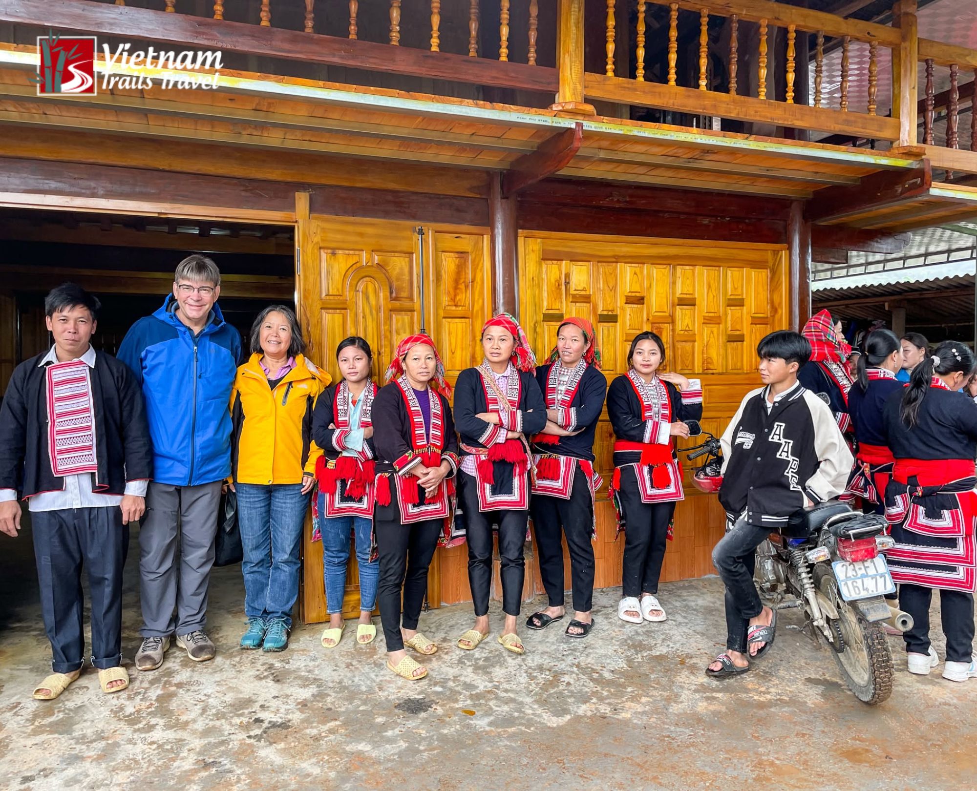 Tourists and ethnic minority hosts posing together outside a wooden homestay with intricate carvings