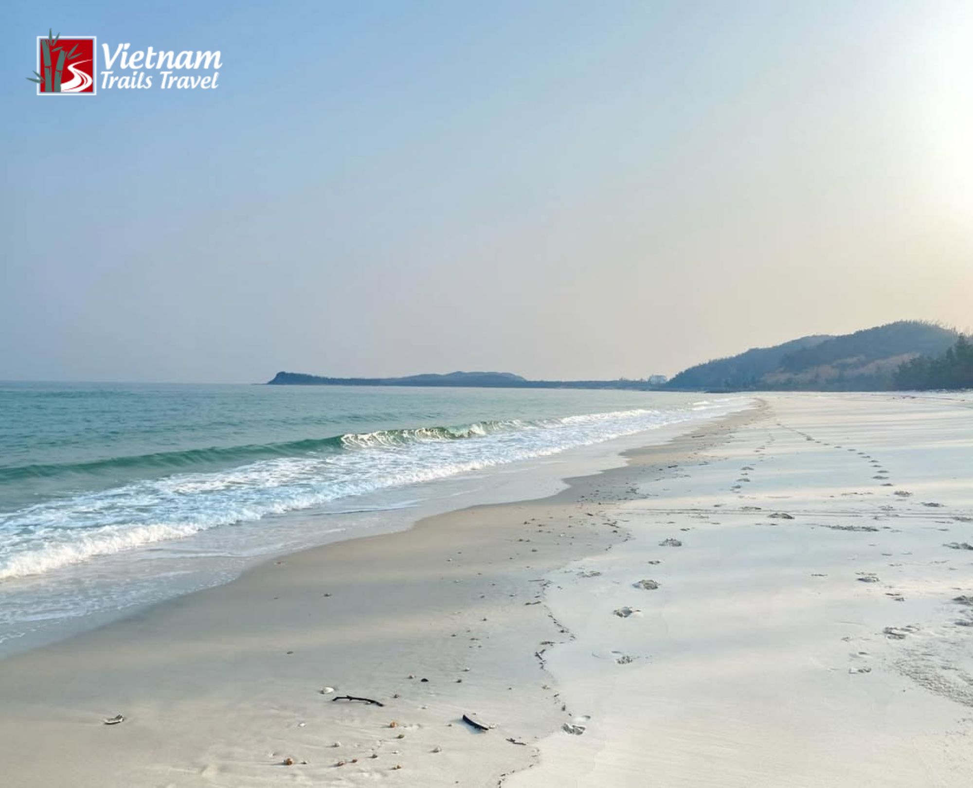Untouched coastal landscape featuring footprints on the shore and calm blue ocean waters